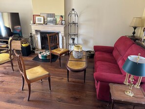 Uma sala de estar com lareira, um sofá vermelho, uma cadeira de madeira, uma mesa e uma televisão.