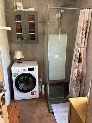 A compact bathroom with a washing machine, a glass shower enclosure, a sink, and a cabinet with towels. - La Maison en Couleurs, quiet village, pleasant garden, near the Loire. (Garchy)