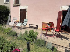 Um pátio externo com deck de madeira, uma mesa com cadeiras e um banco.
