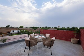 A rooftop terrace with a table and chairs, a potted plant, and a view of buildings and trees. - ELIVAAS Kimaya Suite With Game Zone (Gurugram)