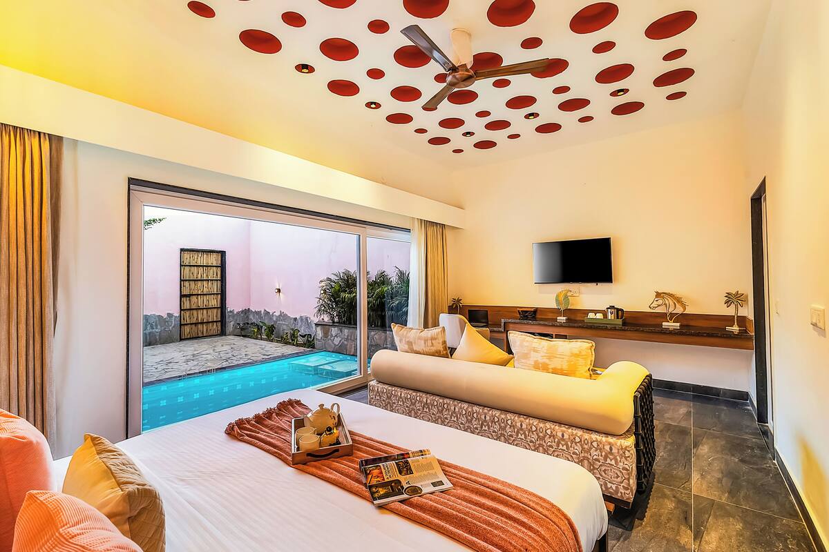 A hotel room with a bed, a TV, a small pool, and a balcony with a view.