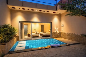 A modern outdoor pool area with a glass-enclosed bedroom, stone walls, and a stone pathway. - ELIVAAS Kimaya Suite With Game Zone (Gurugram)