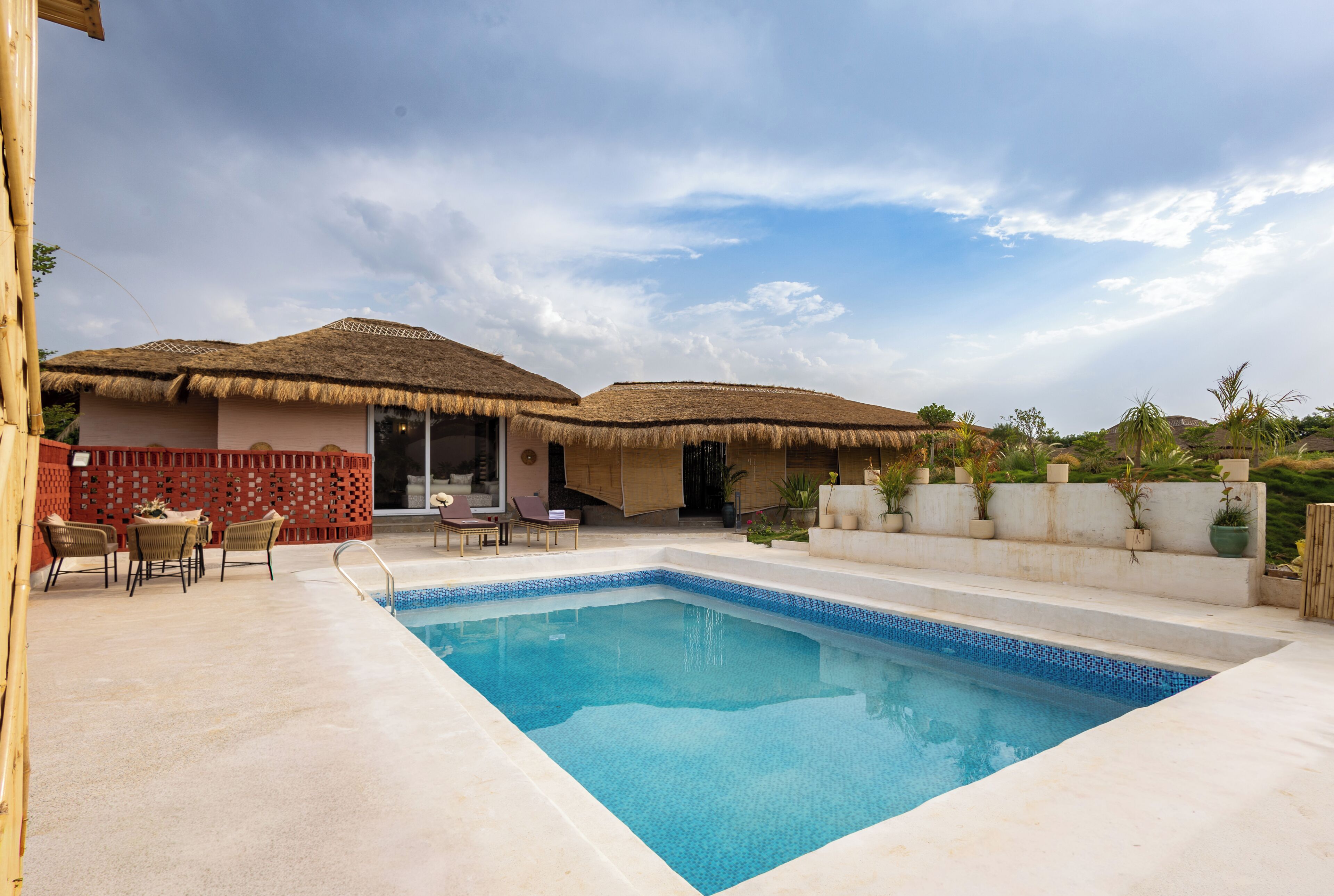 A swimming pool with a tiled edge, surrounded by lounge chairs and a covered seating area.