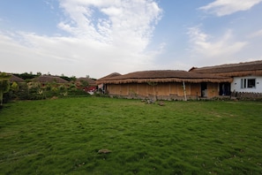 Une maison traditionnelle à toit de chaume, avec une cour verdoyante et un ciel dégagé.