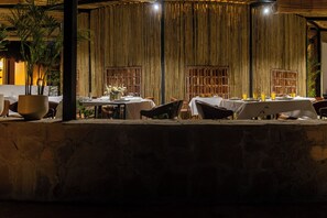 An outdoor dining area with tables set for two, surrounded by a stone wall. - ELIVAAS Kimaya Suite With Game Zone (Gurugram)