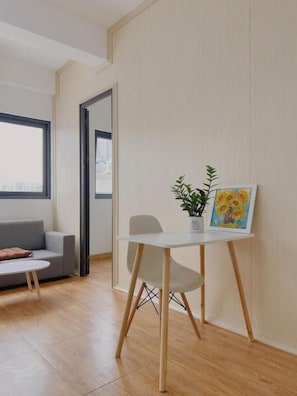 En moderne stue med sofa, et lille bord med en plante og et billede, samt udsigt over byen gennem et vindue.