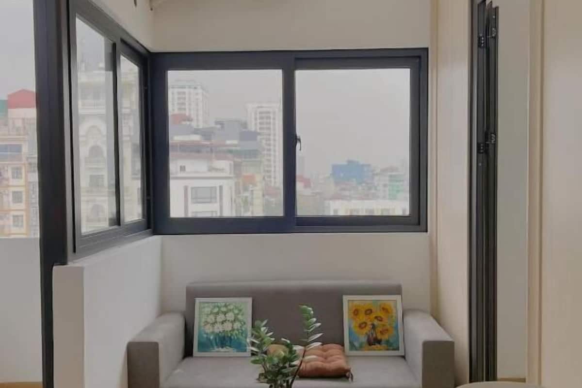 A modern living room with a sofa, a round table, and a large window with a city view.