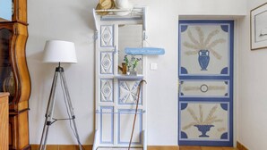 Una habitación con un reloj antiguo, una lámpara, un estante decorativo con un letrero y una puerta con diseño azul y blanco.