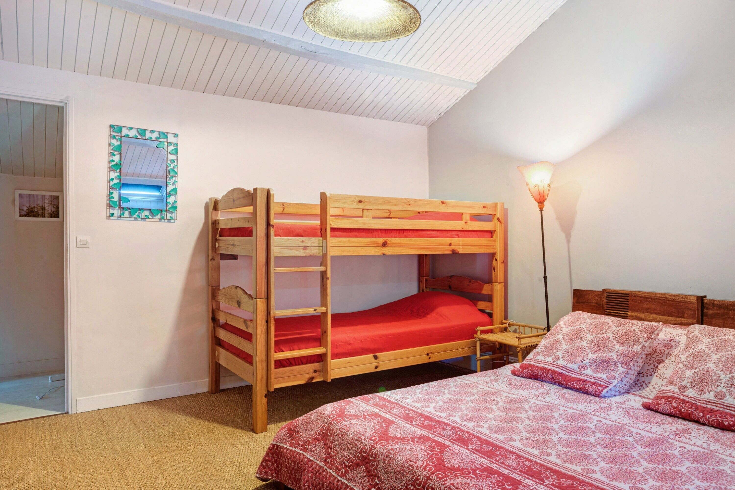 Quarto com beliche, mesa de cabeceira, abajur e colcha estampada.