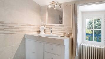 Une salle de bain avec un meuble-lavabo blanc, un grand miroir et une fenêtre donnant sur les arbres.