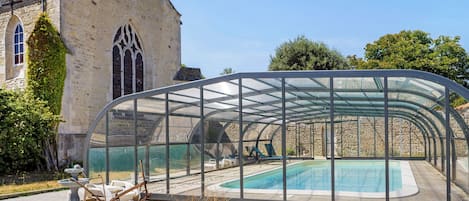 A glass-enclosed swimming pool with a stone building in the background.