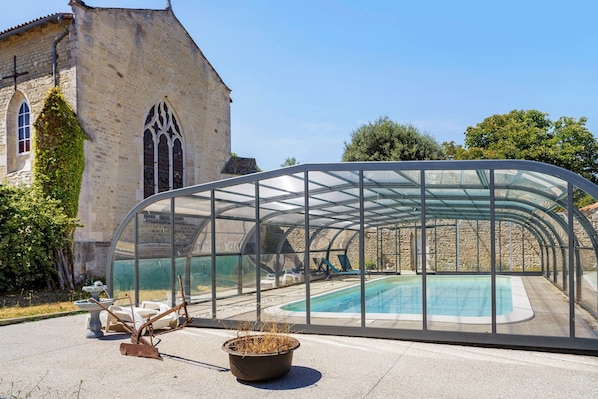 A glass-enclosed swimming pool with a stone building in the background.