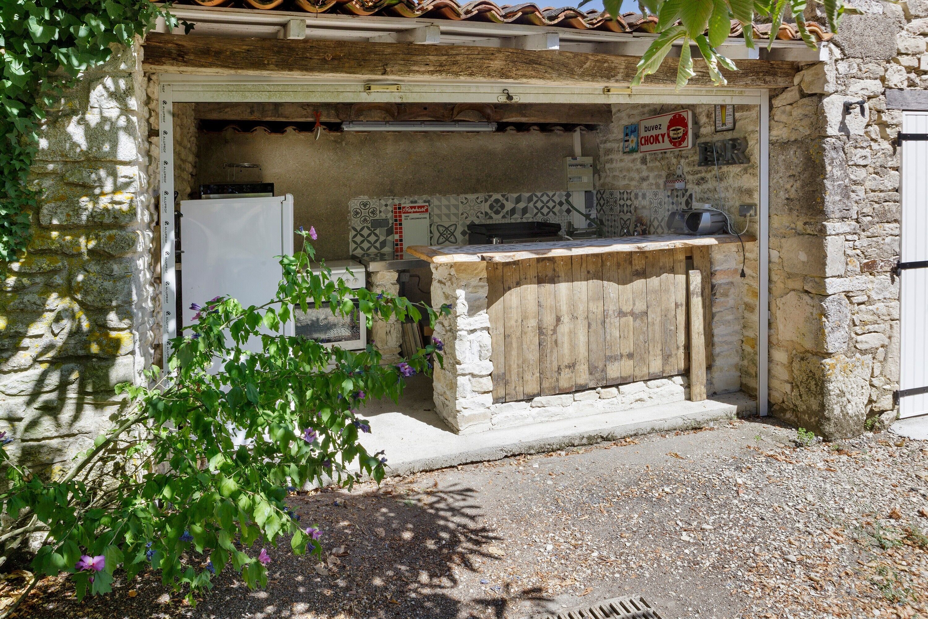 Una cucina esterna rustica con un muro in pietra, un bancone in legno e un frigorifero bianco.