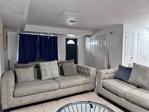 Ein Wohnzimmer mit zwei grauen Sofas, einem Esstisch, blauen Vorhängen und weißen Türen.