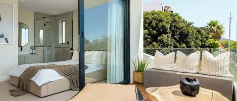 A modern bedroom with a bed, a glass door leading to a balcony, and a seating area with cushions.