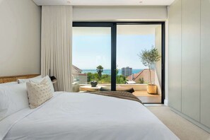 Ein modernes Hotelzimmer mit einem großen Bett, Meerblick und einem Balkon mit Gartenmöbeln.