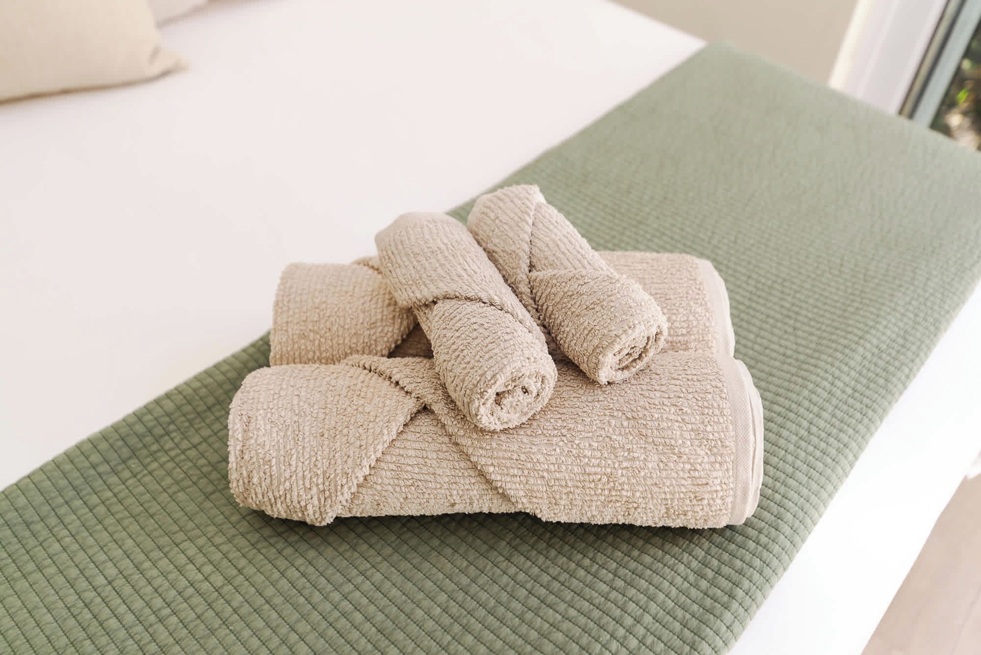 Une serviette beige, soigneusement pliée, est posée sur une surface verte à texture marquée, qui pourrait être un tapis de bain ou un porte-serviettes.
