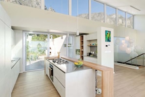 A modern kitchen with a large island, a dining area with a view, and a staircase leading to an upper level. - Golden View Villa | The Ultimate Sunset Escape (Cape Town)