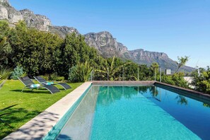 A swimming pool with lounge chairs, surrounded by greenery and mountains in the background. - Golden View Villa | The Ultimate Sunset Escape (Cape Town)