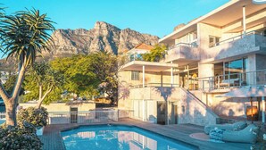 A modern building with a pool, outdoor seating, and a mountain backdrop. - Skyloop Villa | Luxury Living for the Whole Family (Cape Town)