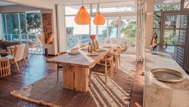 A modern dining area with a wooden table, chairs, and hanging orange pendant lights. - Skyloop Villa | Luxury Living for the Whole Family (Cape Town)