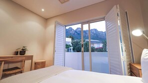 Ein Schlafzimmer mit Bett, Schreibtisch, Stuhl, Lampe und Bergblick durch eine Schiebetür.