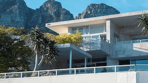A modern building with a flat roof, large windows, and a balcony overlooking a mountainous landscape. - Skyloop Villa | Luxury Living for the Whole Family (Cape Town)