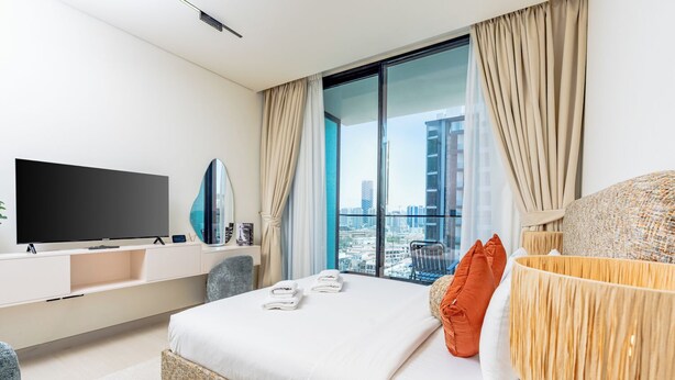 A modern hotel room with a large bed, a flat-screen TV, a city view, and a balcony. - Sophisticated Studio Escape in JVC  (Dubai)