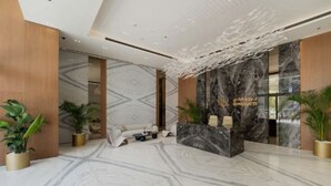 A modern reception area with marble flooring, a reception desk, seating area, and potted plants. - Sophisticated Studio Escape in JVC  (Dubai)