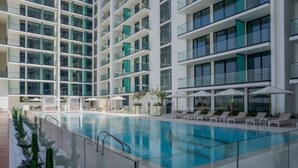 A modern hotel with a central swimming pool, multiple balconies, and sun loungers. - Sophisticated Studio Escape in JVC  (Dubai)