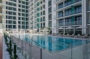 Ein modernes Hotel mit einem zentral gelegenen Schwimmbad, mehreren Balkonen und Liegestühlen.