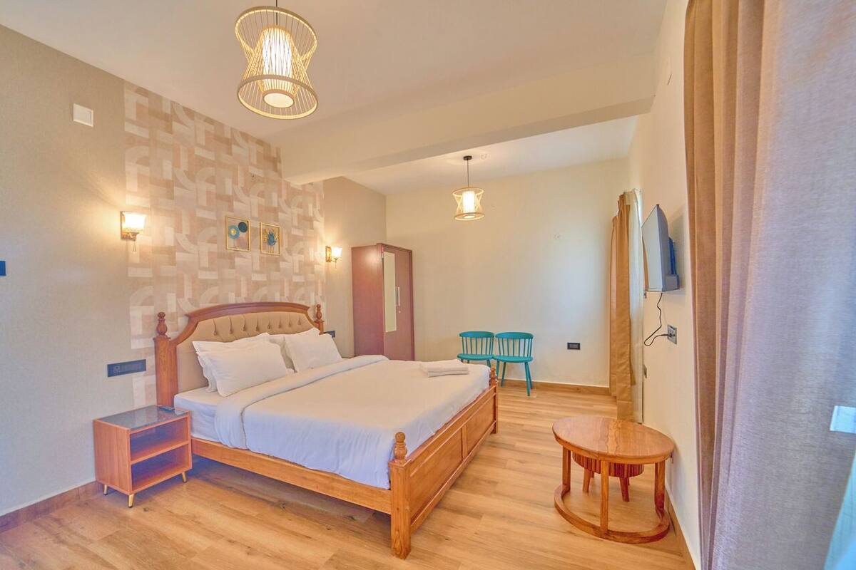 A bedroom with a wooden bed, bedside tables, a small round table, and a wall-mounted TV.