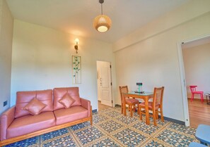 Una sala de estar con un sofá, una mesa de comedor con sillas, un piso estampado y una puerta que da a otra habitación.