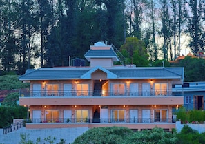 A two-story building with a balcony on each floor, a staircase leading to the entrance, and a view of the surrounding trees.