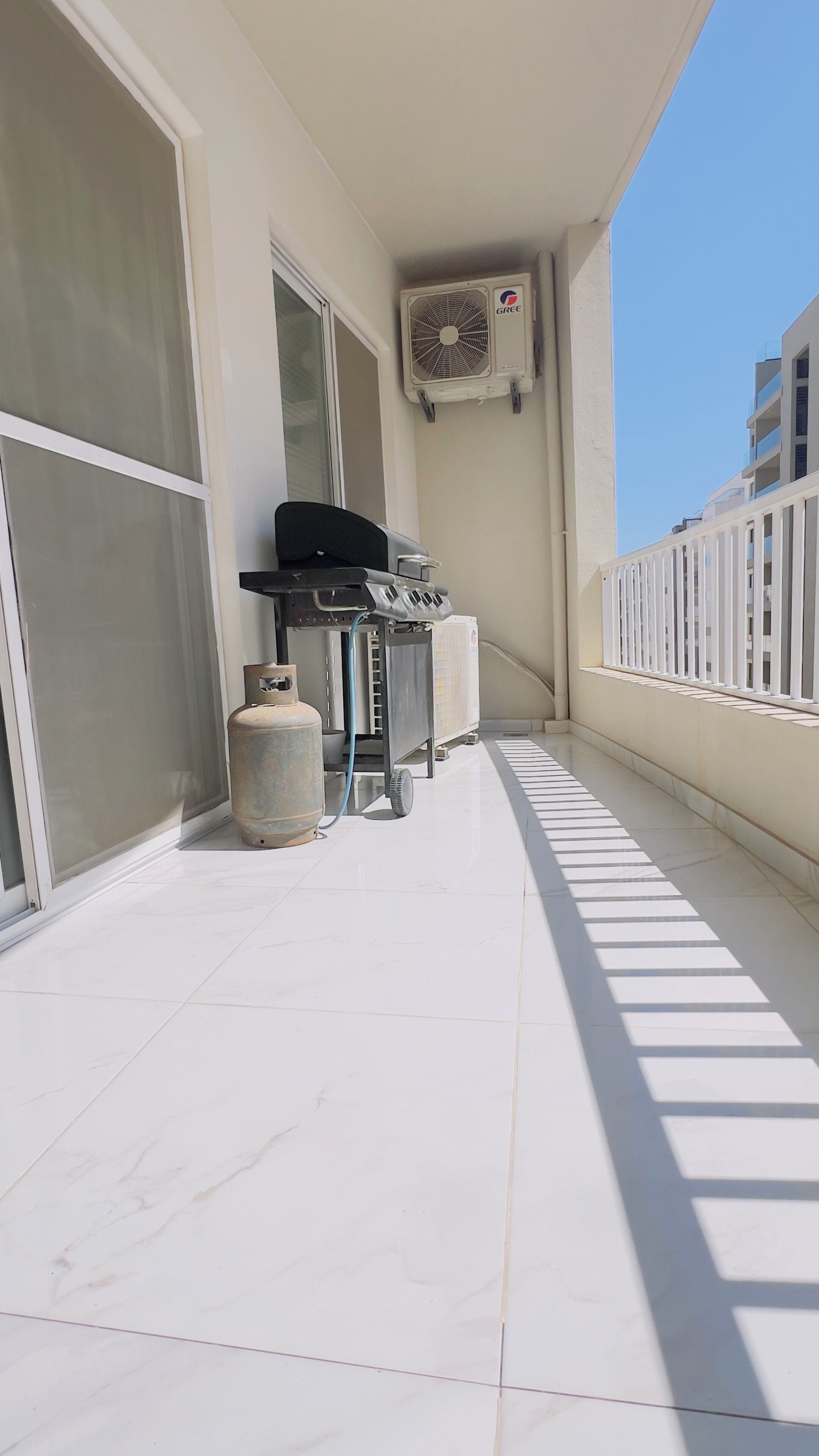 A balcony with a grill, a gas cylinder, and an air conditioning unit.