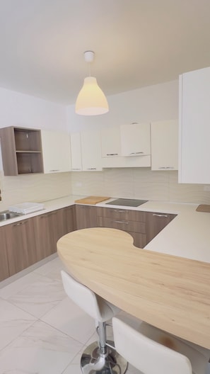 Une cuisine moderne avec des meubles blancs, un plan de travail en bois et un luminaire suspendu.