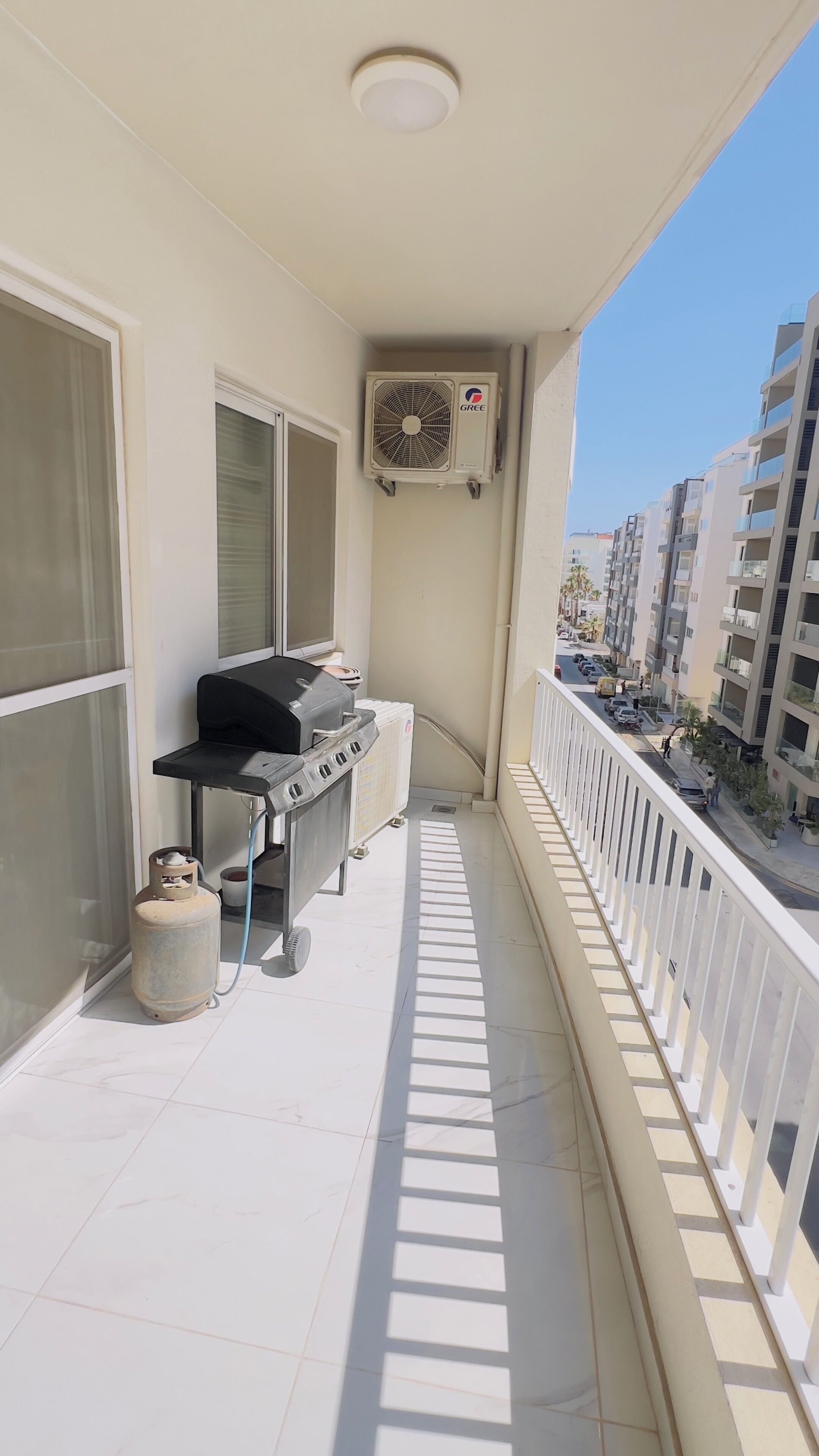Un balcon avec un barbecue, un ventilateur et une vue sur la ville.