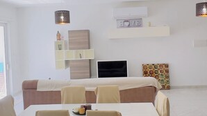 Una sala de estar moderna con comedor, un sofá, un televisor y adornos en las paredes.