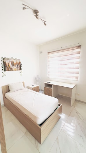 Quarto com cama, mesa de cabeceira, escrivaninha, cadeira e janela com persianas.