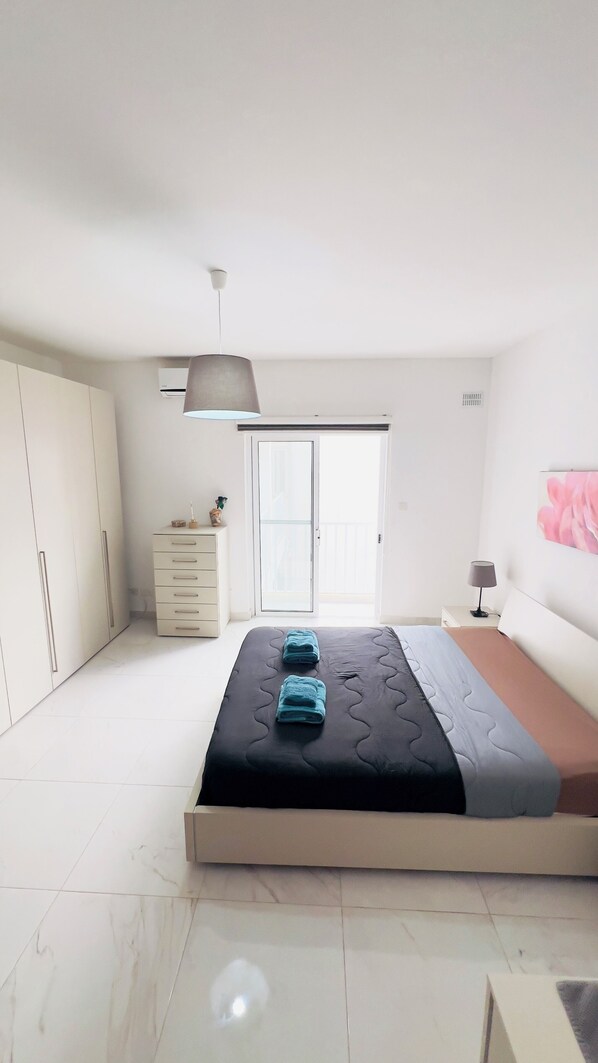 A bedroom with a bed, a dresser, a wardrobe, a ceiling light, and a sliding glass door. - 8 Delphi Court (San Pawl il-Baħar)