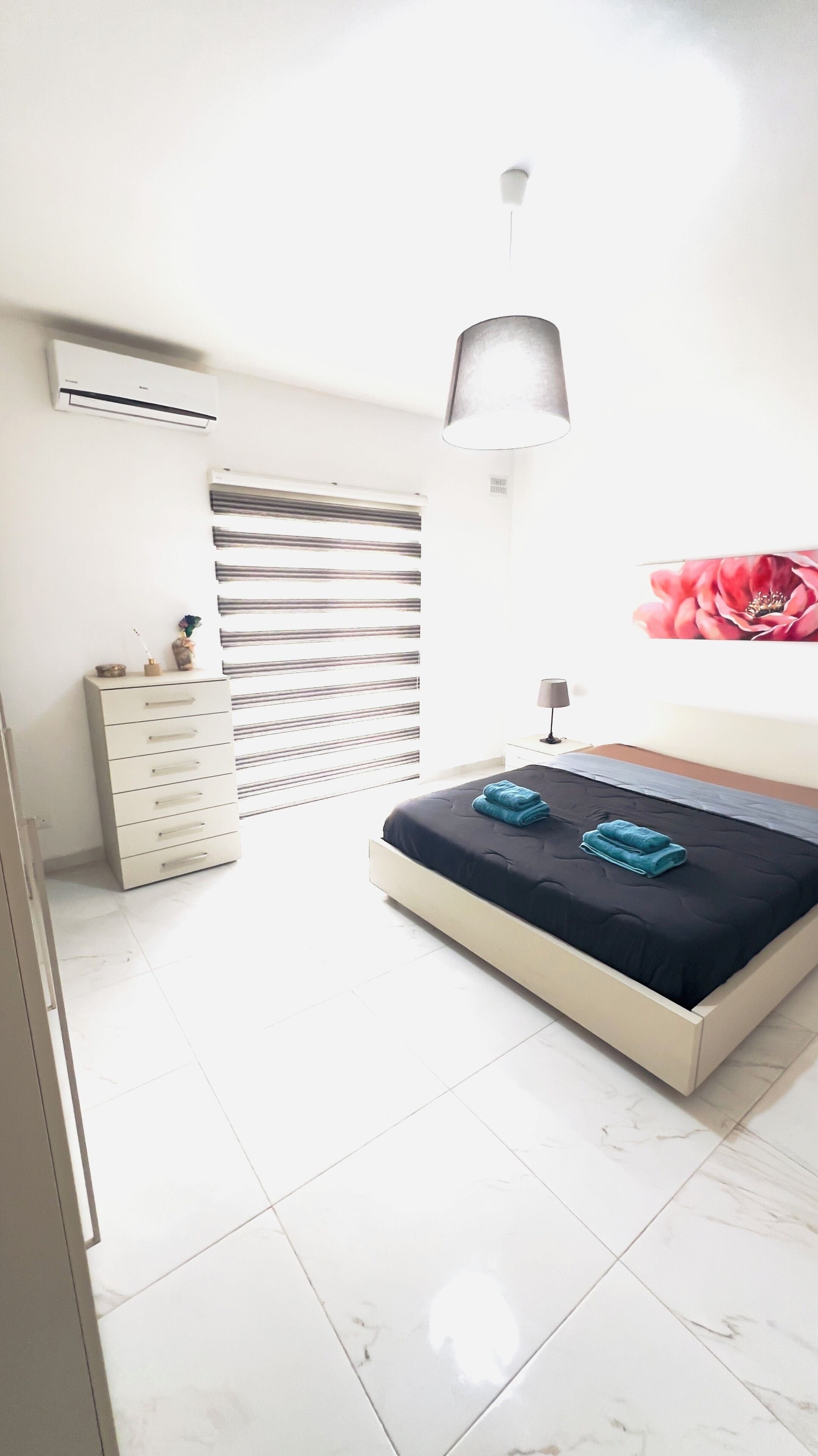 Quarto com cama, cômoda, ar condicionado, abajur e parede com pintura floral.