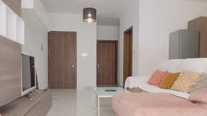 Una sala de estar moderna con un televisor de pantalla plana, un sofá rosa, una mesita y una lámpara colgante.