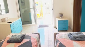 Un dormitorio con dos camas, un armario, una mesita de noche, un espejo y una puerta corrediza de vidrio que da a un balcón.