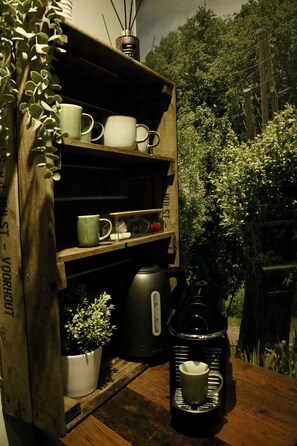Une étagère en bois rustique, sur laquelle on peut voir divers objets, notamment des tasses, une plante en pot, une machine à café et un diffuseur.