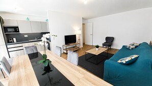 Una sala de estar moderna con comedor, sofá, televisor y zona de cocina.