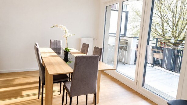 Un comedor con una mesa y sillas de madera, una planta en maceta y vistas al exterior.