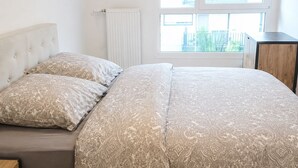 Un dormitorio con cama, dos almohadas, un radiador y una ventana con vistas.