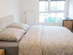 Een slaapkamer met een bed, twee kussens, een radiator en een raam met uitzicht.