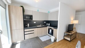 Une cuisine moderne équipée d’un four à micro-ondes, d’un four et d’un évier, une petite table en bois avec un téléviseur, et une fenêtre avec des stores.