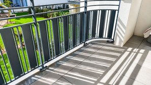 Een balkon met een metalen hekwerk, betegelde vloer en uitzicht op een groen gazon.